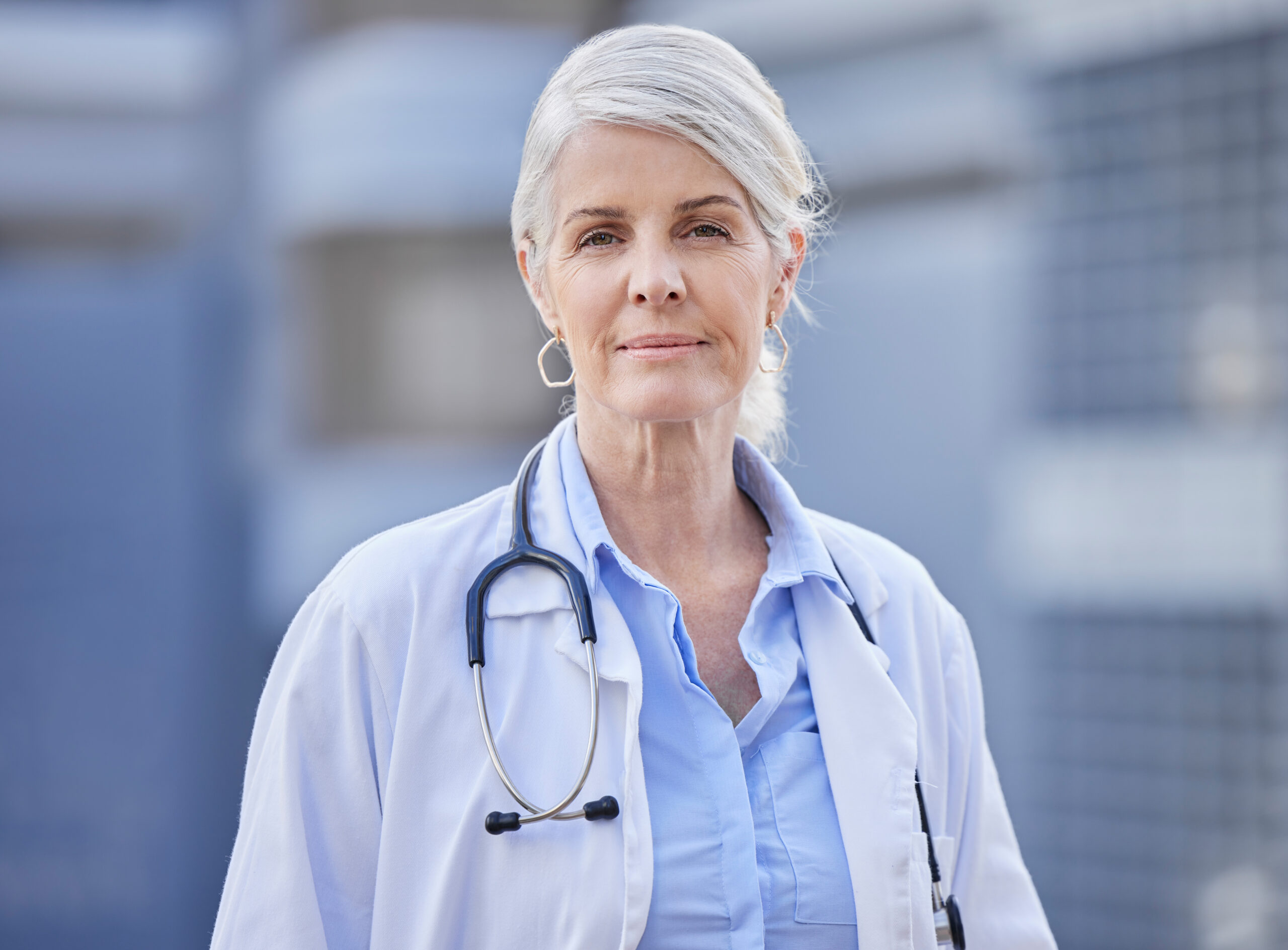 Shot of a mature female doctor standing with her arms crossed against a city background.