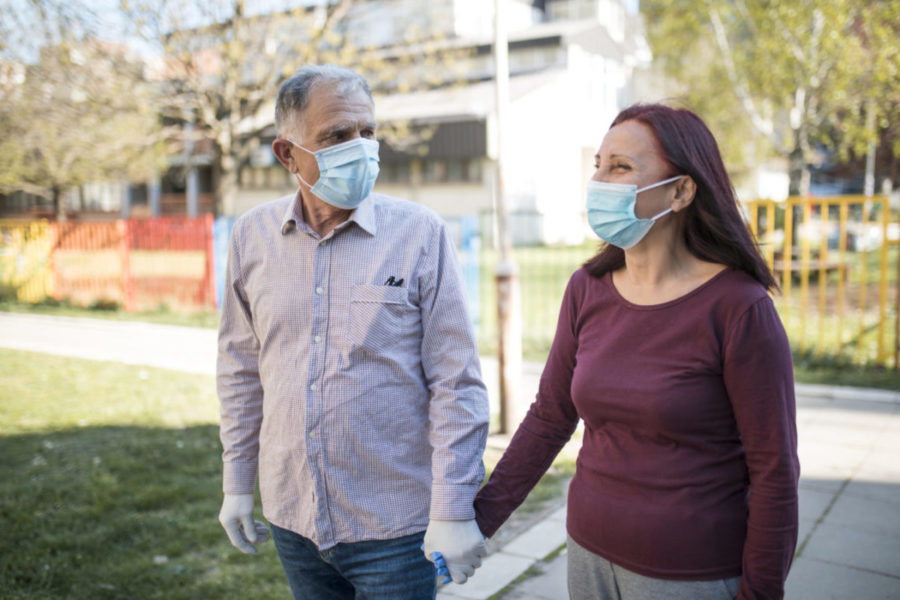 Two older couples with protective masks and gloves walking down the street together during the Coronavirus epidemic